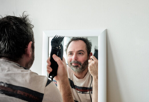 Mature Man Cutting His Own Grey Hair With A Clipper At Home During Coronavirus Isolation.