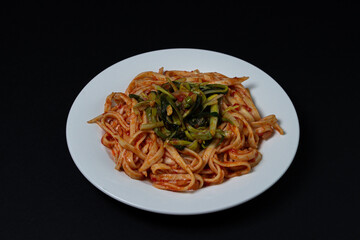 Spaghetti in tomato sauce on a dark background. Spaghetti with a vegetable side dish on a black background. Italian food. Tasty food