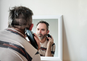 Mature man cutting his own grey hair with a clipper at home during coronavirus isolation.