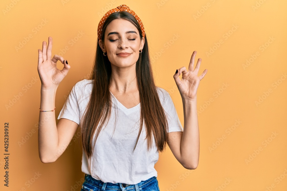 Wall mural Beautiful brunette young woman wearing casual white t shirt relax and smiling with eyes closed doing meditation gesture with fingers. yoga concept.