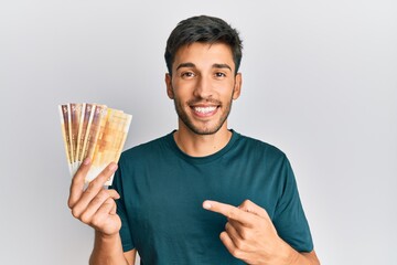 Young handsome man holding 500 norwegian krone banknotes smiling happy pointing with hand and finger