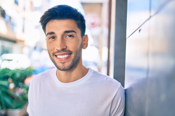 Young latin man smiling happy leaning on the wall at the city.