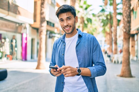 Young latin man smiling happy using smartphone walking at the city.