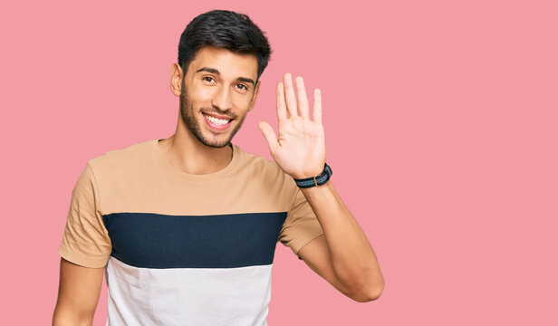 Young handsome man wearing casual clothes waiving saying hello happy and smiling, friendly welcome gesture