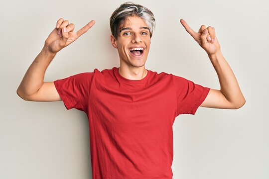 Young hispanic man wearing casual clothes smiling amazed and surprised and pointing up with fingers and raised arms.