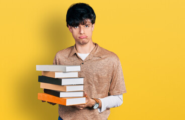 Handsome hipster young man holding a pile of books depressed and worry for distress, crying angry and afraid. sad expression.