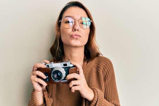 Young caucasian woman holding vintage camera looking at the camera blowing a kiss being lovely and sexy. love expression.