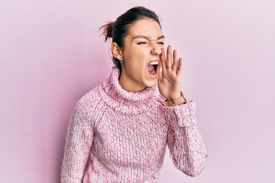 Young caucasian woman wearing wool winter sweater shouting and screaming loud to side with hand on mouth. communication concept.