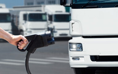 Hand with charging plug on a background of electric truck. Concept	