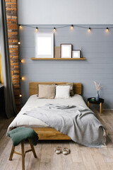Double bed with natural natural accents on the sheets and beige pillows in the grey Scandinavian bedroom, copy space on the paintings on the shelf above the bed