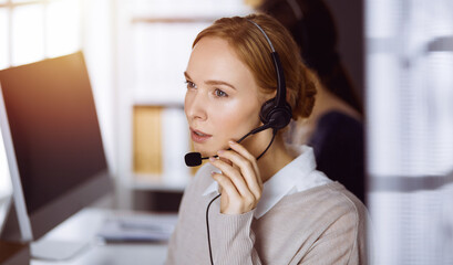 Businesswoman talking by headset in office. Call center and diverse people group in business