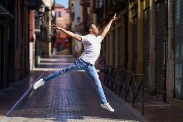 Happy black guy doing an acrobatic jump in the middle of the street.