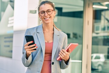Young blonde businesswoman smiling happy using smartphone at the city.