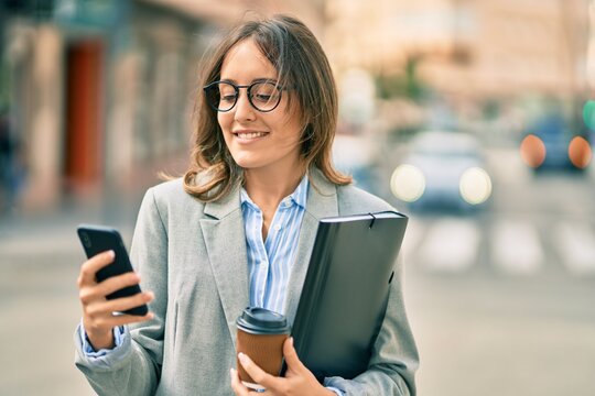 Young hispanic businesswoman using smartphone and drinking take away coffee at the city.