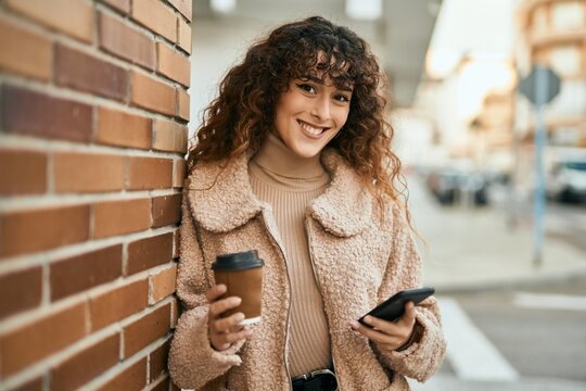 Young hispanic woman smiling happy using smartphone and drinking coffee at the city