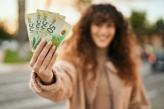 Young hispanic woman smiling happy holding israel shekels banknotes at the city