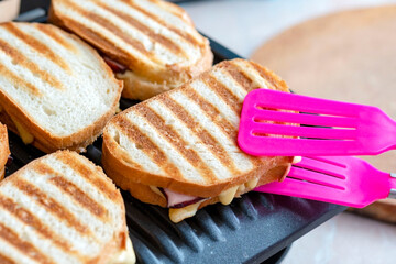 Fried toasts with cheese. The silicone shovel takes toasts from a grill. toasted bread, sandwich on an electric grill. Fried toasts with orphaned and ham.