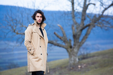 Image of young beautiful man with long hair wearing rain jacket in cold weather. Thinker european man in spring nature.