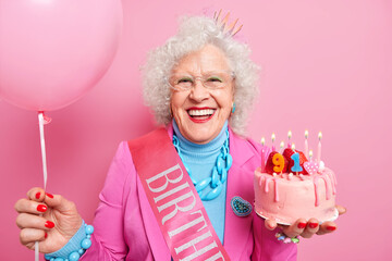 Special occasion age and festivity concept. Happy smiling wrinkled senior woman holds festive...