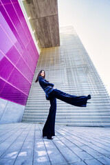 Wide-angle photo of a woman wearing blue suit posing near a modern building.