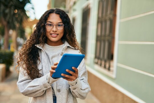 Young latin woman smiling happy using touchpad at the city.