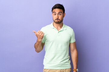 Young handsome man isolated on purple background unhappy and pointing to the side
