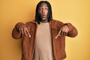 African american man with braids wearing brown retro jacket pointing down with fingers showing advertisement, surprised face and open mouth