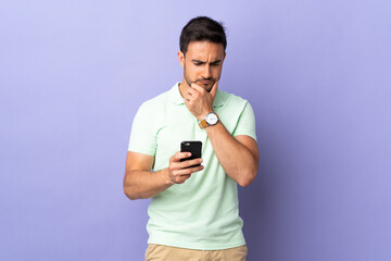 Young handsome man isolated on purple background thinking and sending a message