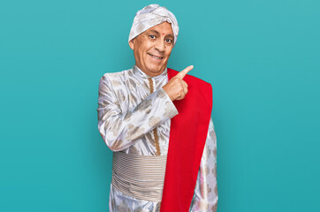 Senior hispanic man wearing tradition sherwani saree clothes cheerful with a smile of face pointing with hand and finger up to the side with happy and natural expression on face