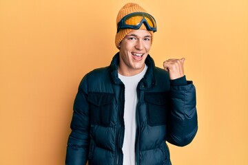 Handsome caucasian man wearing snow wear and sky glasses pointing thumb up to the side smiling happy with open mouth