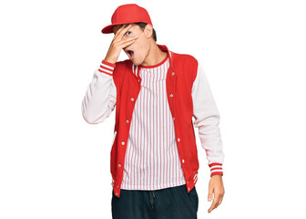 Handsome caucasian man wearing baseball uniform peeking in shock covering face and eyes with hand, looking through fingers with embarrassed expression.