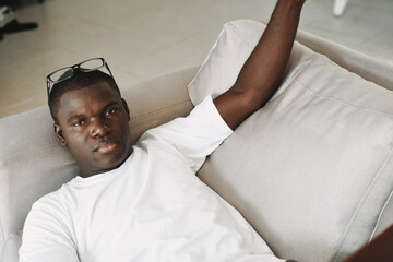 Obraz premium an african man lies on a sofa with glasses on his head and a white t-shirt top view
