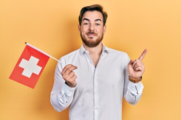 Handsome caucasian man with beard holding switzerland flag smiling happy pointing with hand and...