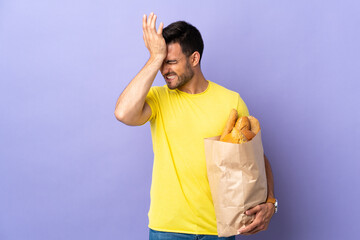 Young caucasian man holding a bag full of breads isolated on purple background having doubts with confuse face expression