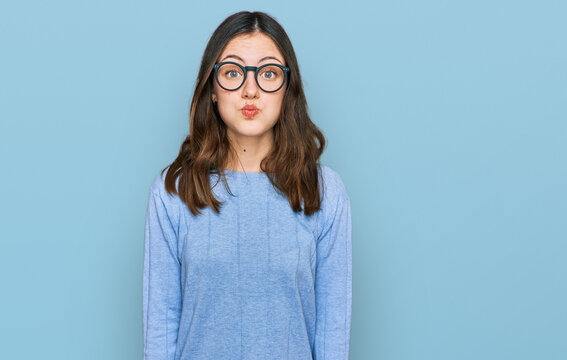 Young beautiful woman wearing casual clothes and glasses puffing cheeks with funny face. mouth inflated with air, crazy expression.