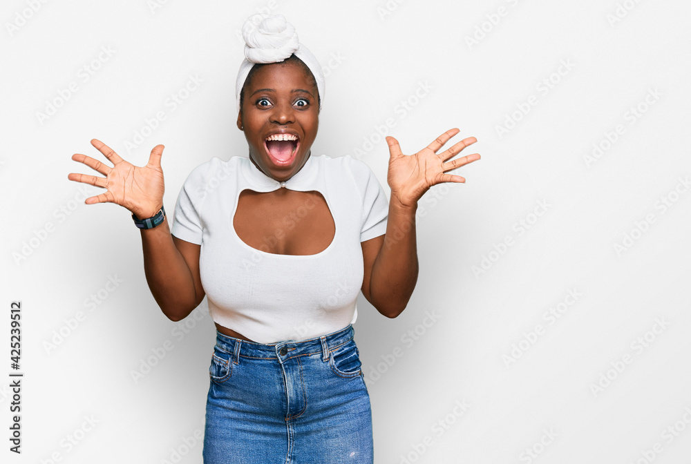 Wall mural Young african woman with turban wearing hair turban over isolated background celebrating crazy and amazed for success with arms raised and open eyes screaming excited. winner concept