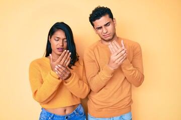 Beautiful latin young couple wearing casual clothes together suffering pain on hands and fingers, arthritis inflammation