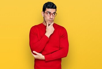Handsome hispanic man wearing casual clothes and glasses with hand on chin thinking about question, pensive expression. smiling with thoughtful face. doubt concept.