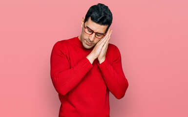 Fototapeta premium Handsome hispanic man wearing casual clothes and glasses sleeping tired dreaming and posing with hands together while smiling with closed eyes.