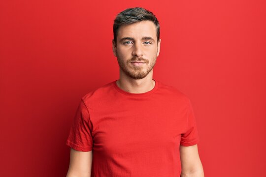 Handsome caucasian man wearing casual red tshirt relaxed with serious expression on face. simple and natural looking at the camera.