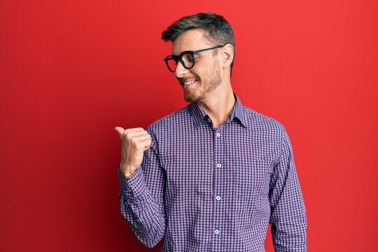Handsome caucasian man wearing business shirt and glasses pointing thumb up to the side smiling happy with open mouth