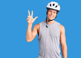Young handsome man wearing bike helmet showing and pointing up with fingers number three while smiling confident and happy.