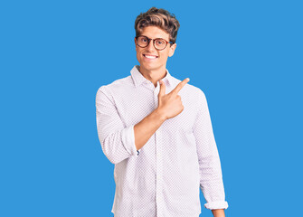 Young handsome man wearing business clothes and glasses cheerful with a smile on face pointing with hand and finger up to the side with happy and natural expression