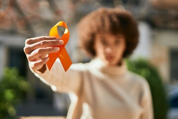 Young hispanic girl with serious expression holding orange awareness ribbon at the city.