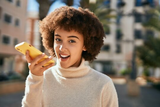Young hispanic girl smiling happy sending voice message using smartphone at the city.
