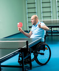 Adult disabled man in a wheelchair training before play at table tennis