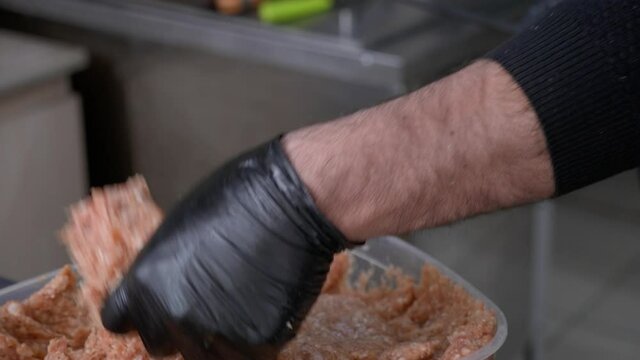 The chef sticks forcemeat on the skewer and forming it for cooking lula kebab on a grill at a commercial kitchen. Close-up hands in black gloves 