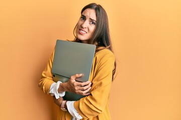 Fototapeta premium Young beautiful woman holding laptop clueless and confused expression. doubt concept.