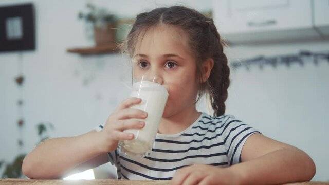 little girl child drinking milk. healthy eating a child eating breakfast kid dream concept. daughter girl in kitchen drinks yogurt milk and licks her lips. positive kid kefir smiling having breakfast