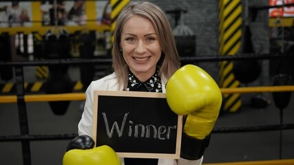 A businesswoman in a boxing gloves holds a board with the inscription WINNER. - Powered by Adobe